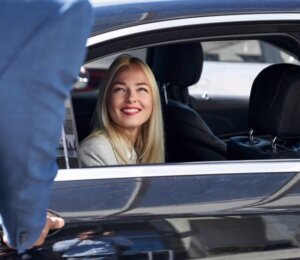 Smiling woman in luxury black car receiving chauffeur service – Cumming limo service by KLEO.